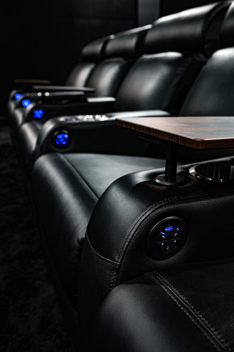 Reclining cinema seat with a swing-out tray table and lit cup-holders.
